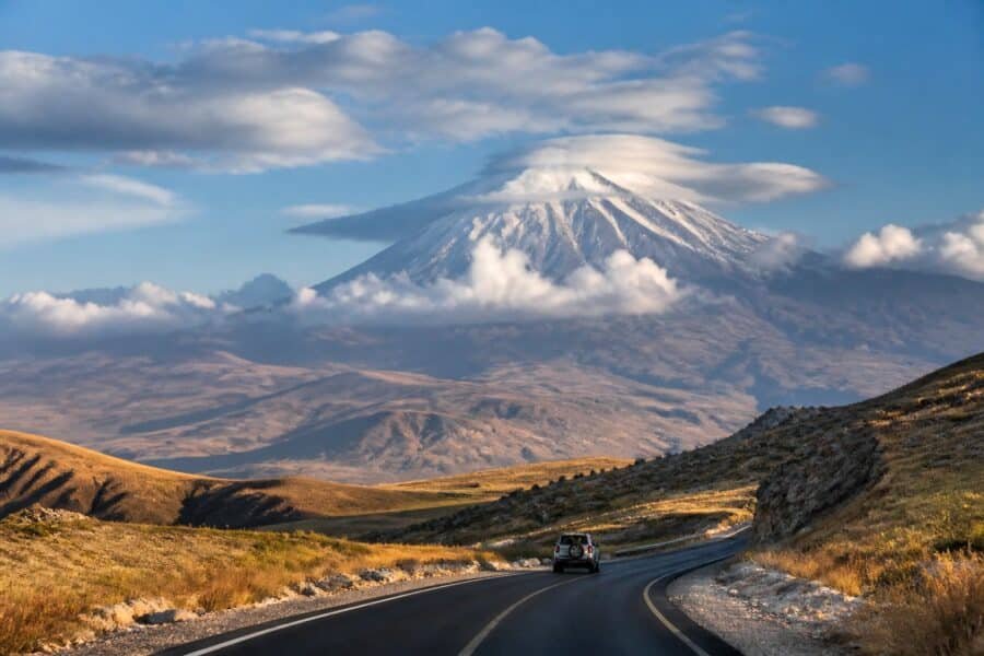 Estrada atravessando uma paisagem montanhosa em direção ao Monte Ararat coberto de neve.